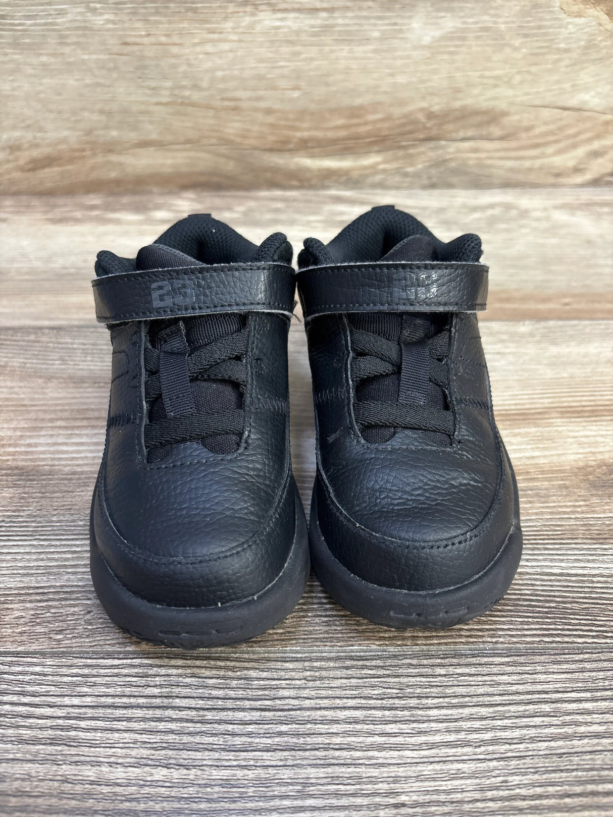 Front view of Jordan Max Aura 3 TD Black Anthracite toddler sneakers size 9c showcasing hook and loop strap and pebbled leather on wood plank background