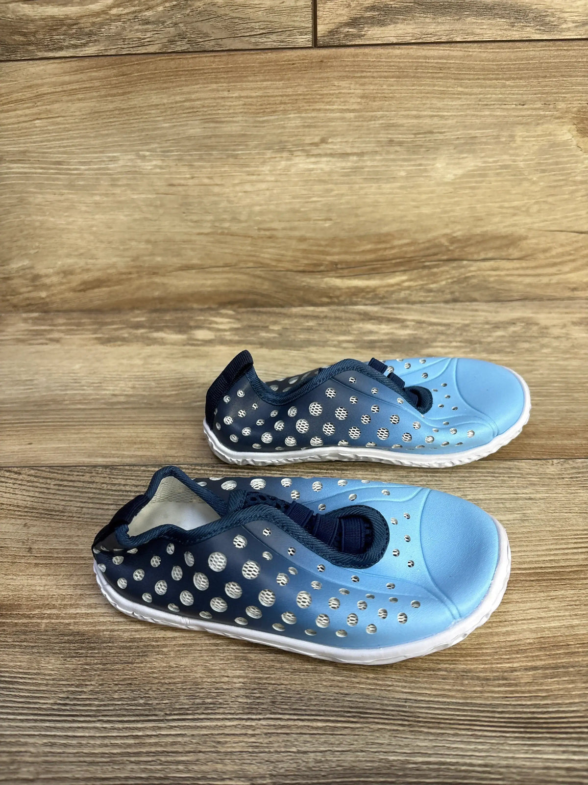 Top-down view of children's Fires Barefoot blue quick-dry water shoes showing perforated breathable upper and white sole on wooden floor