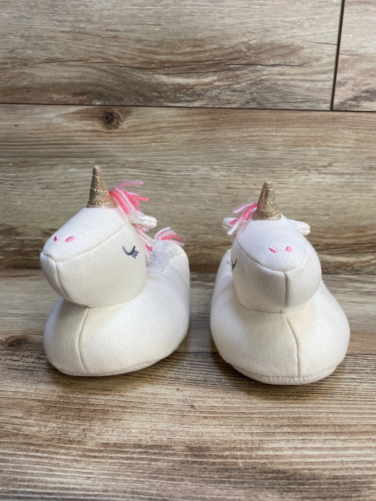 Pair of white unicorn baby slippers with pink accents and gold horns on wooden floor