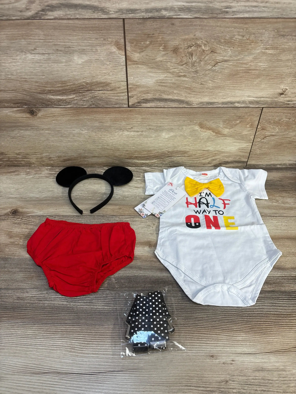 Flat lay of 4pc set: white onesie with yellow bow and Half Way To One text, red bloomers, mouse ears, dotted suspenders