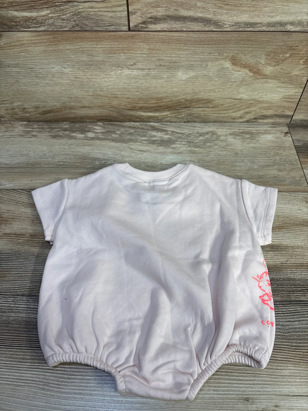 Front view of Baby Gap x Peter Rabbit pink bubble romper showcasing side graphic and elasticized leg openings on a wood-grain background