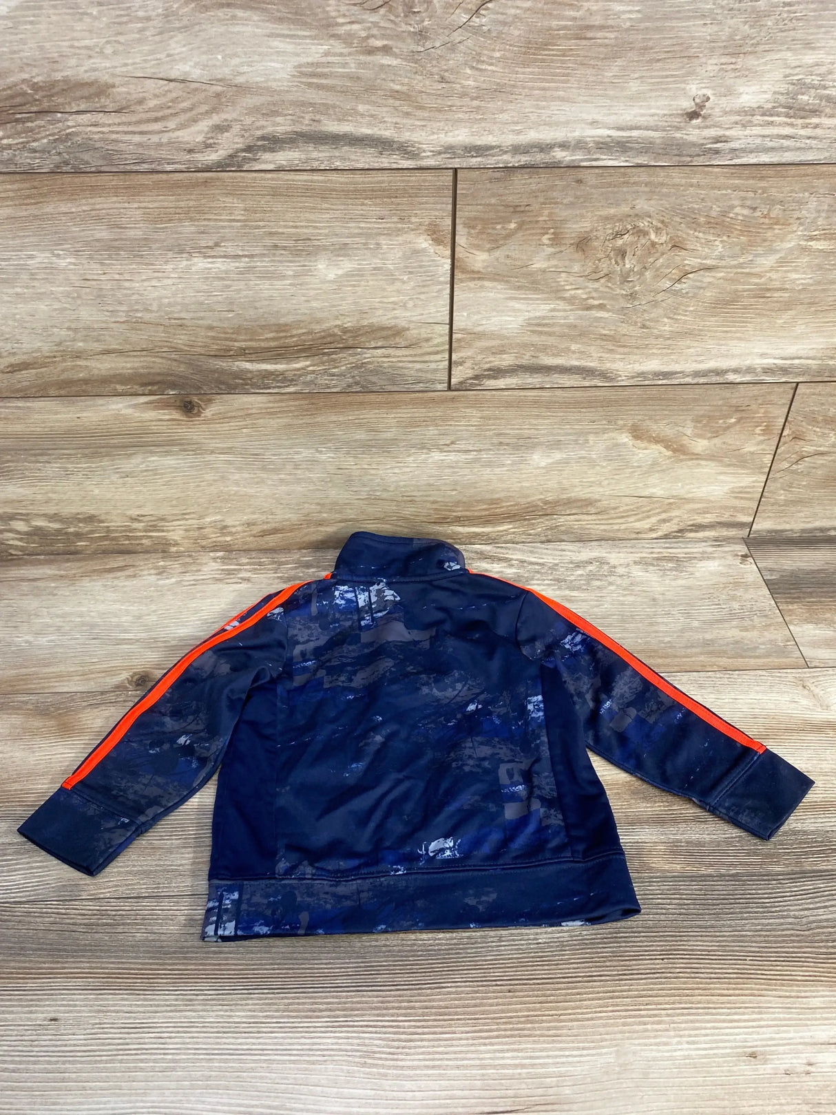 Back view of Adidas toddler track jacket size 18 months, navy with orange shoulder stripes and camo accents on wood floor
