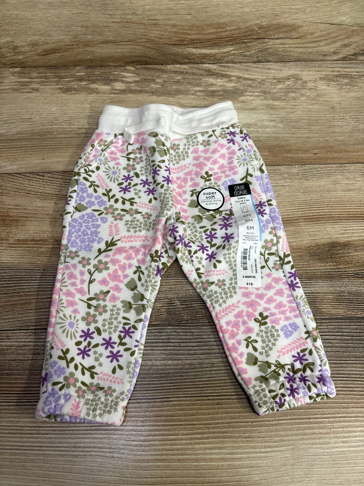 Okie Dokie baby pants size 6 months with soft floral pattern in pink, purple, and green on wooden surface