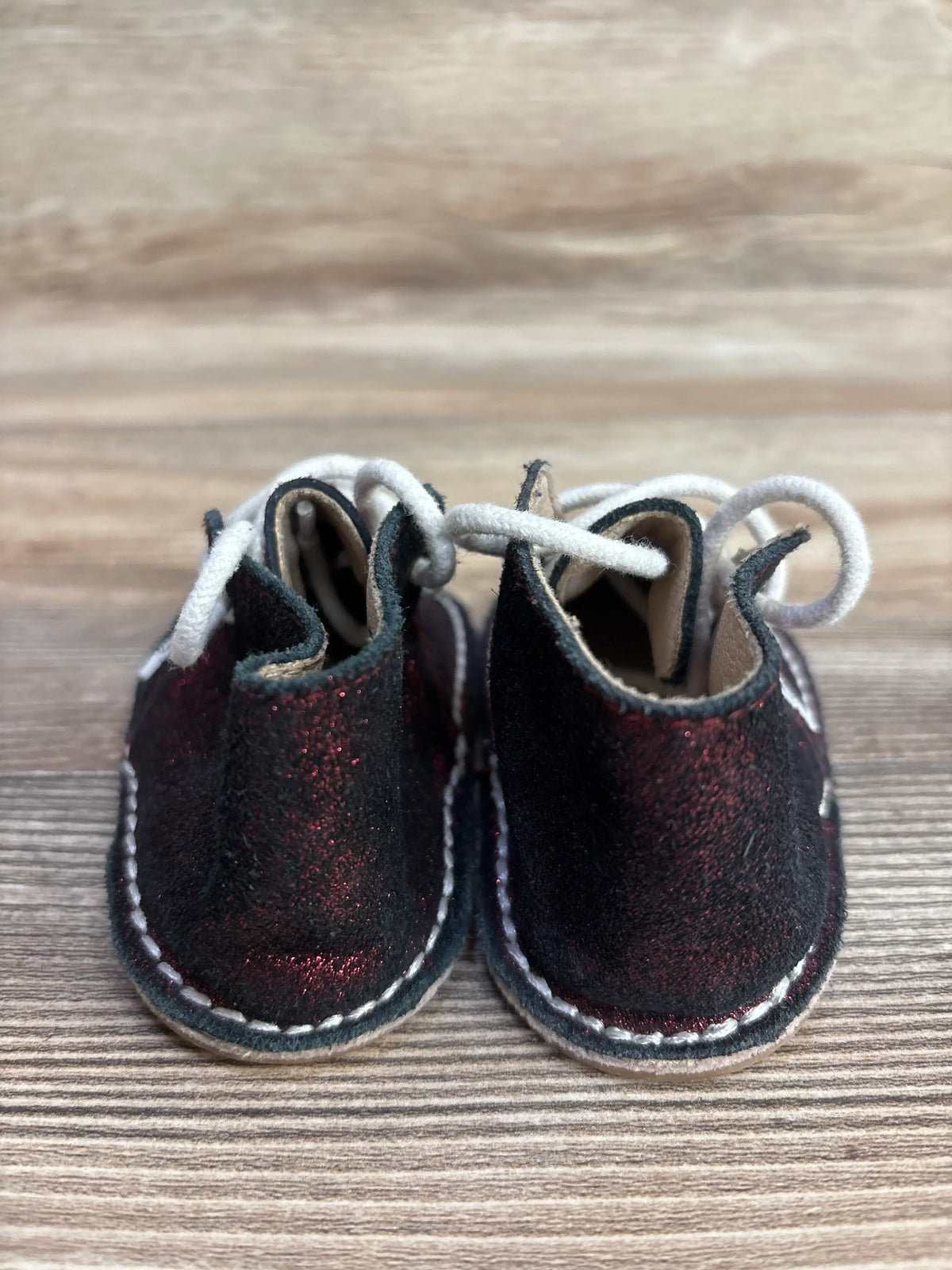 Pair of children's black and red glitter leather baby shoes with white laces on wooden surface
