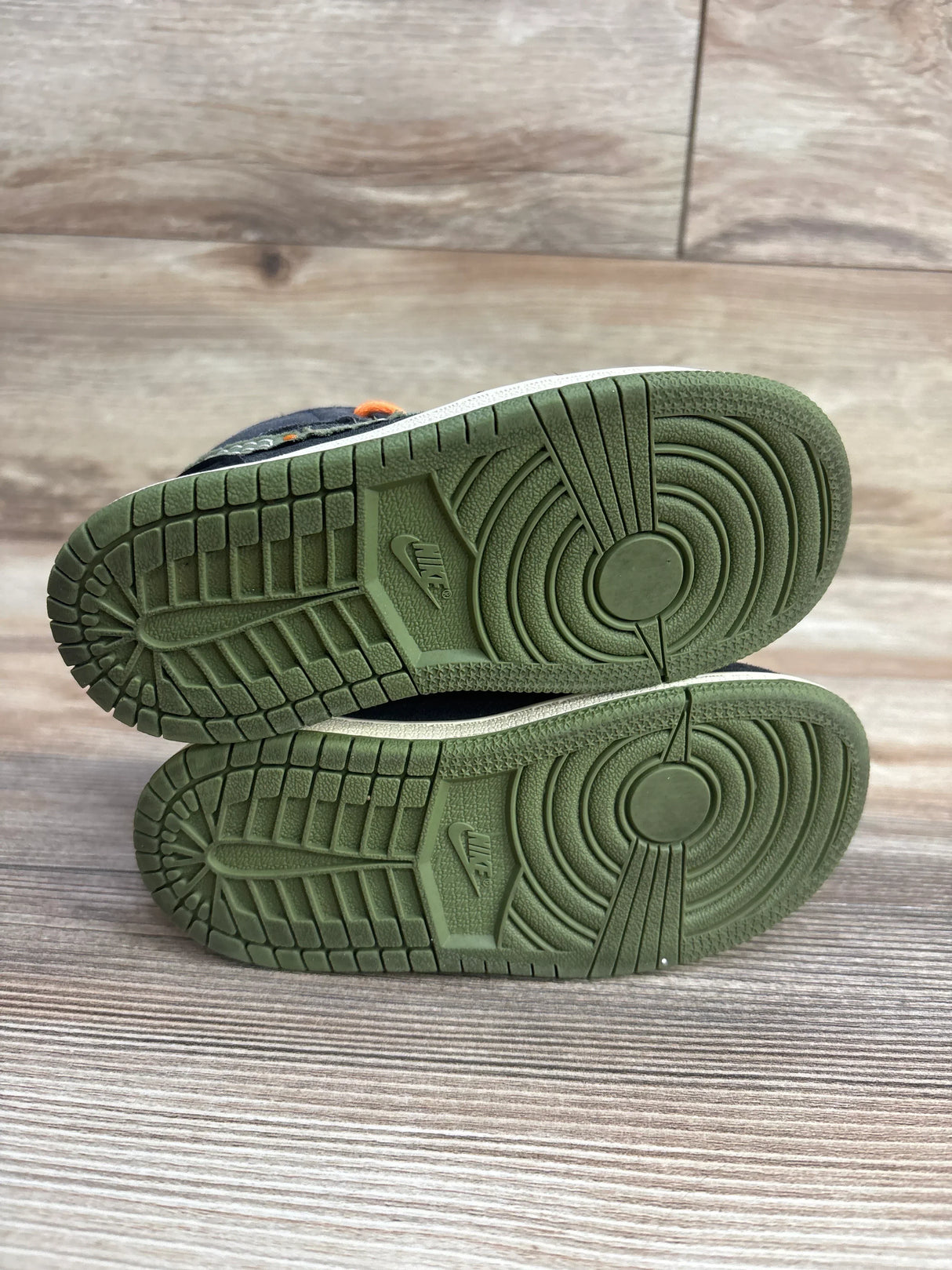 Kids' Nike sneakers with olive green rubber soles, gently used, on wooden floor