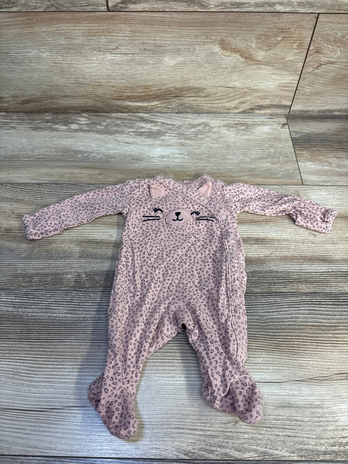 Front view of Carter’s pink kimono cat sleeper showcasing leopard spots, cat face, and footed legs on a wood-look floor