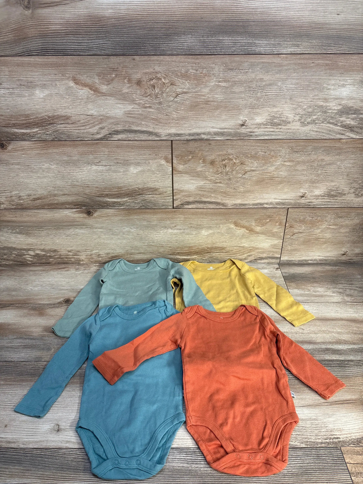Top view of Honest Baby 4pk long sleeve bodysuit set in teal, blue, yellow, and rust on a wood background