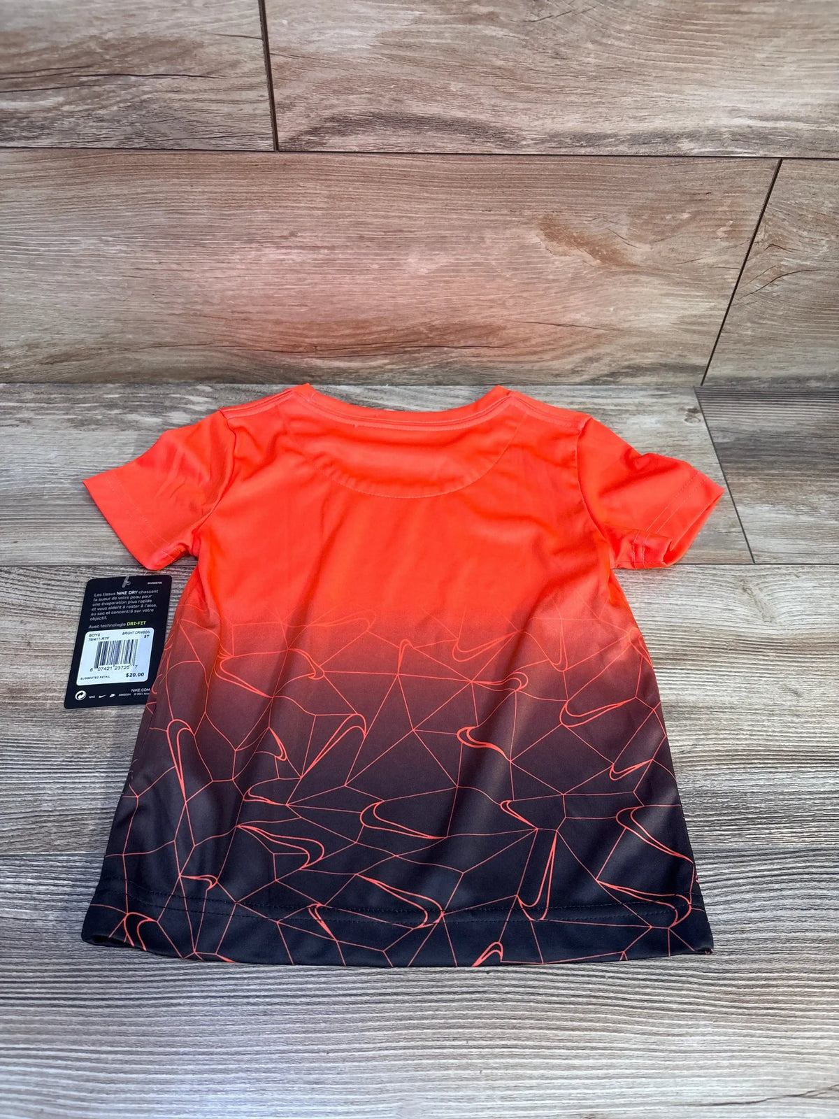 Back view of Nike Dri-FIT toddler shirt (3T) showing orange-to-black gradient and abstract Nike swoosh pattern on wood floor