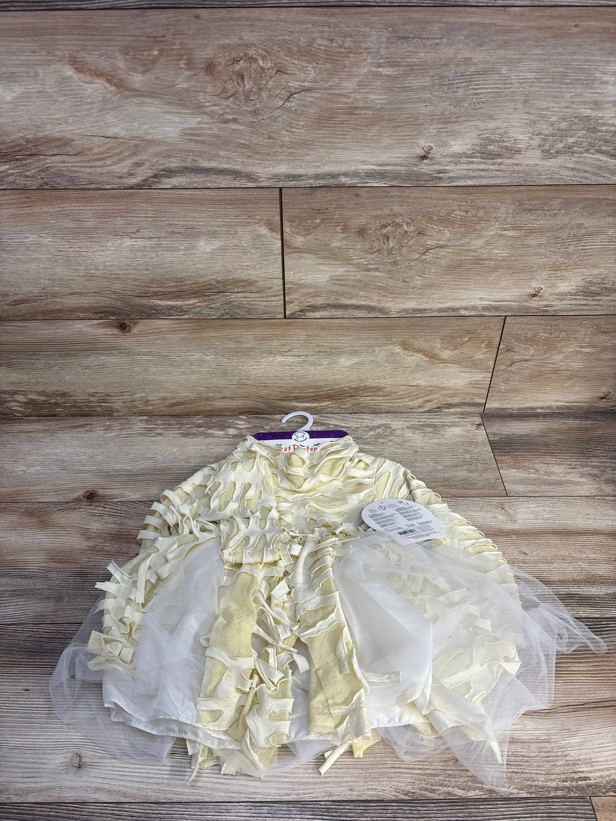 Front view of Great Pretenders toddler mummy costume with cream wrapped strips, tulle skirt and headpiece on wood background