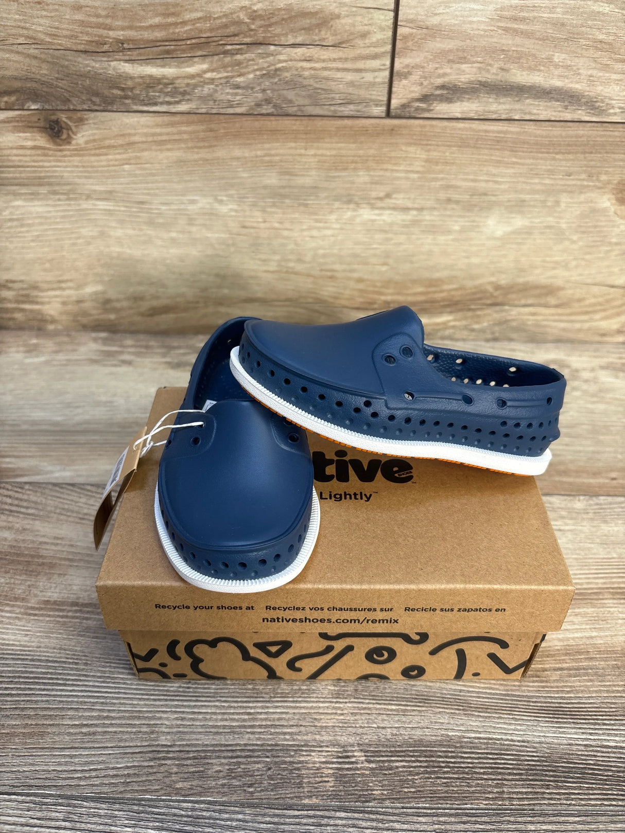 Angled front of Native Howard Sugarlite kids slip-on shoes in navy showing perforated sides and white soles on a recycled shoebox