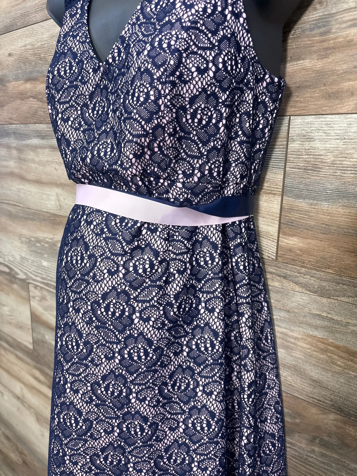 Front close-up of Motherhood Gender Reveal lace maternity dress in navy, floral lace over pink lining with two ribbons