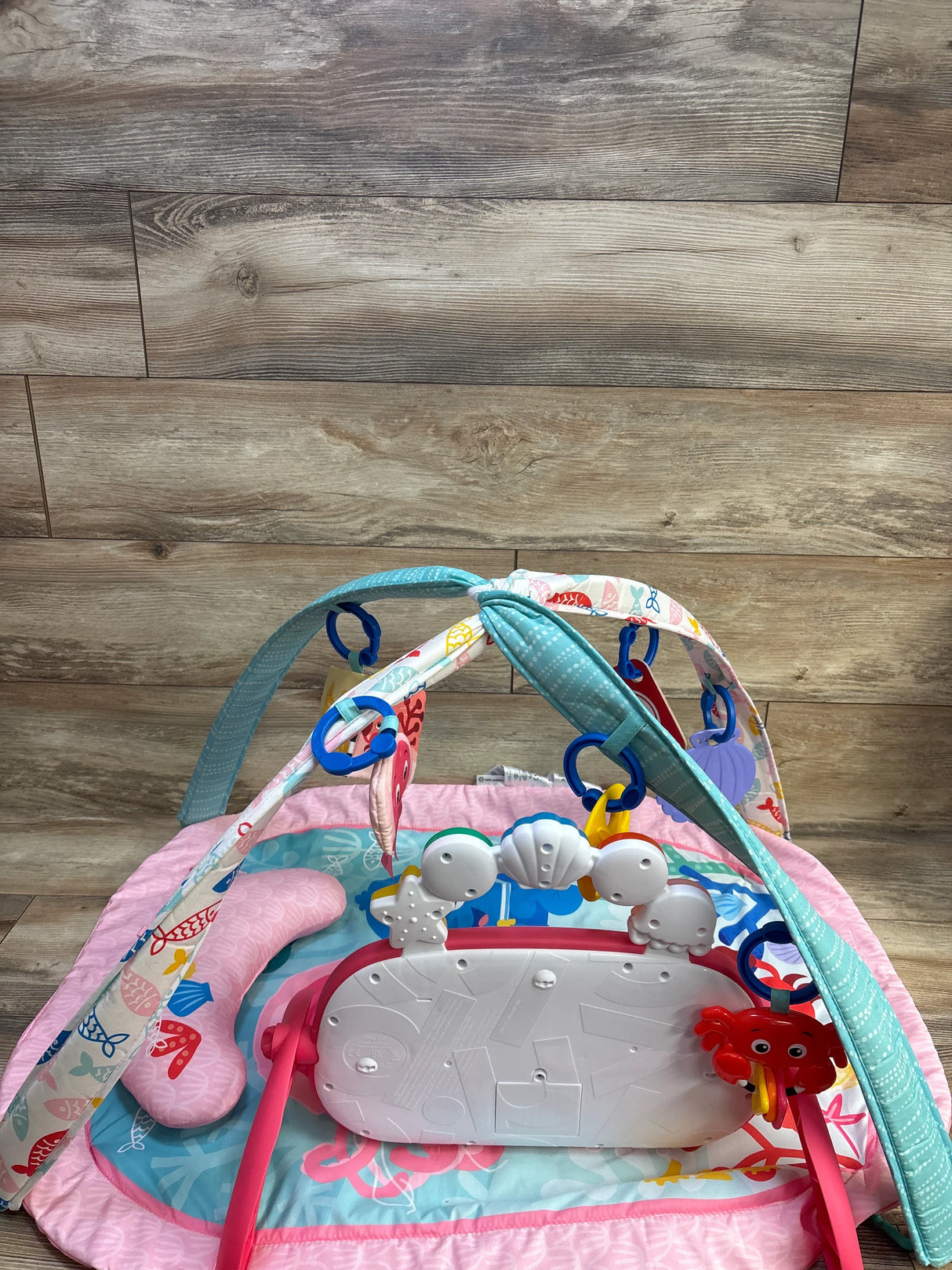Angled view of Baby Einstein activity gym with crossed arches, hanging sea toys, and detachable kick piano on ocean mat