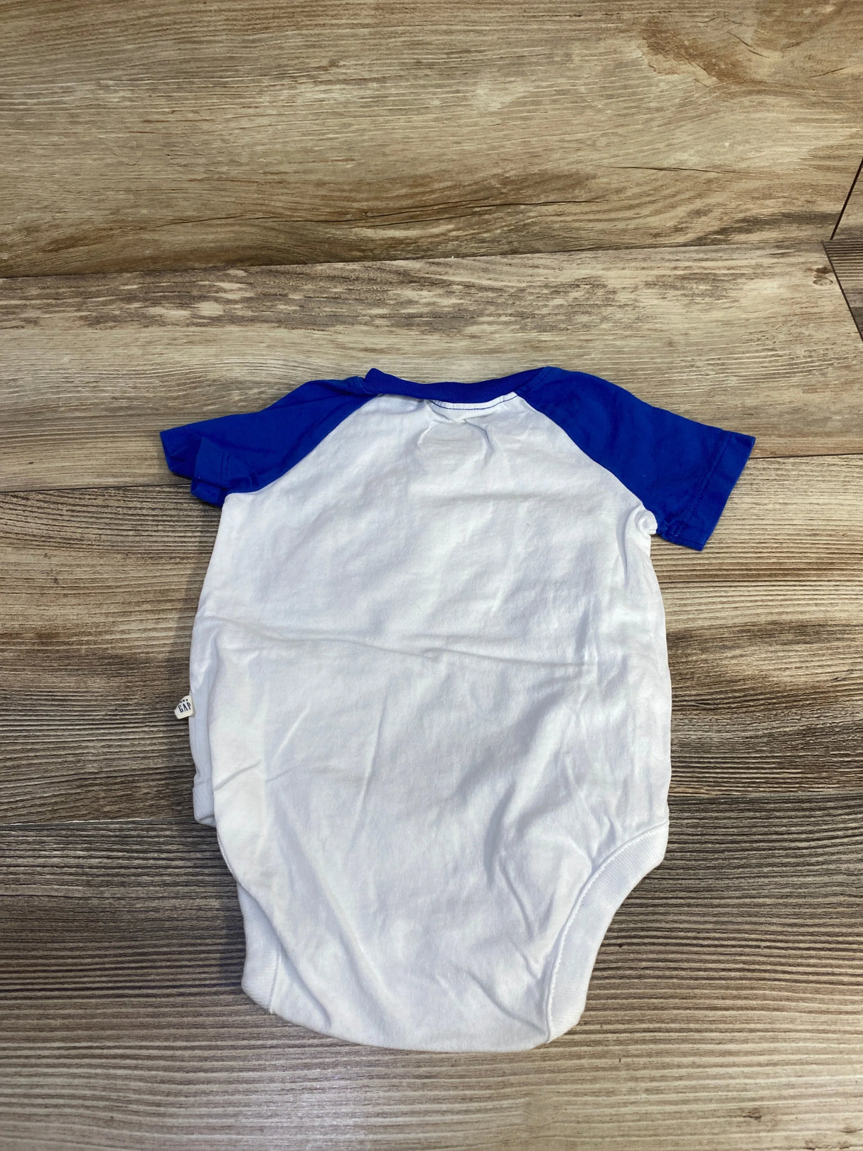 Flat-lay of Baby Gap short-sleeve bodysuit showing white body and royal blue raglan sleeves on wood background