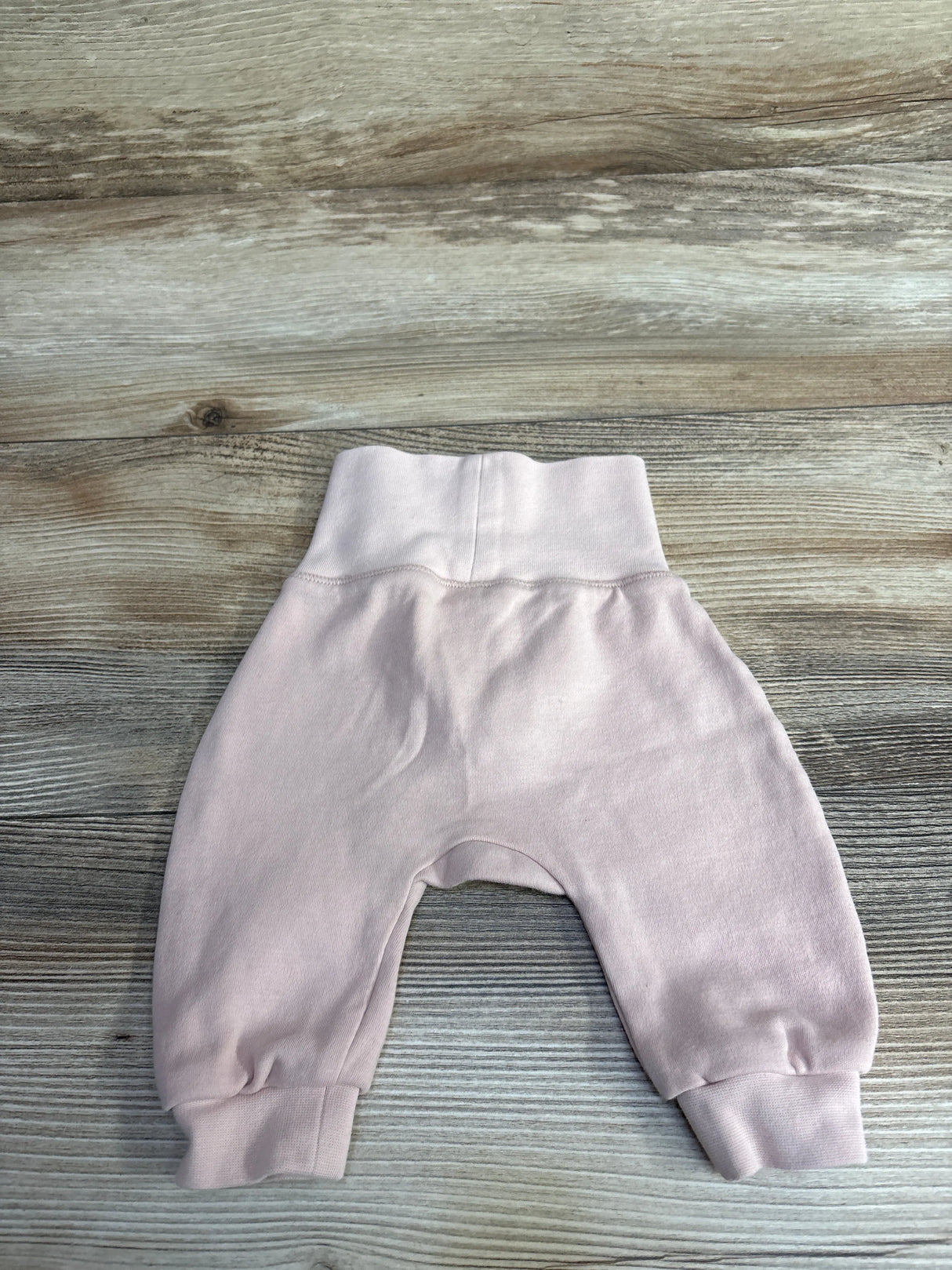 Soft pink baby pants with cuffed ankles and stretchy waistband on wooden surface