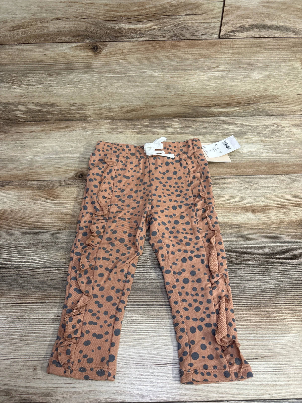 Infant brown polka dot ruffle pants with drawstring, laid flat on wooden background