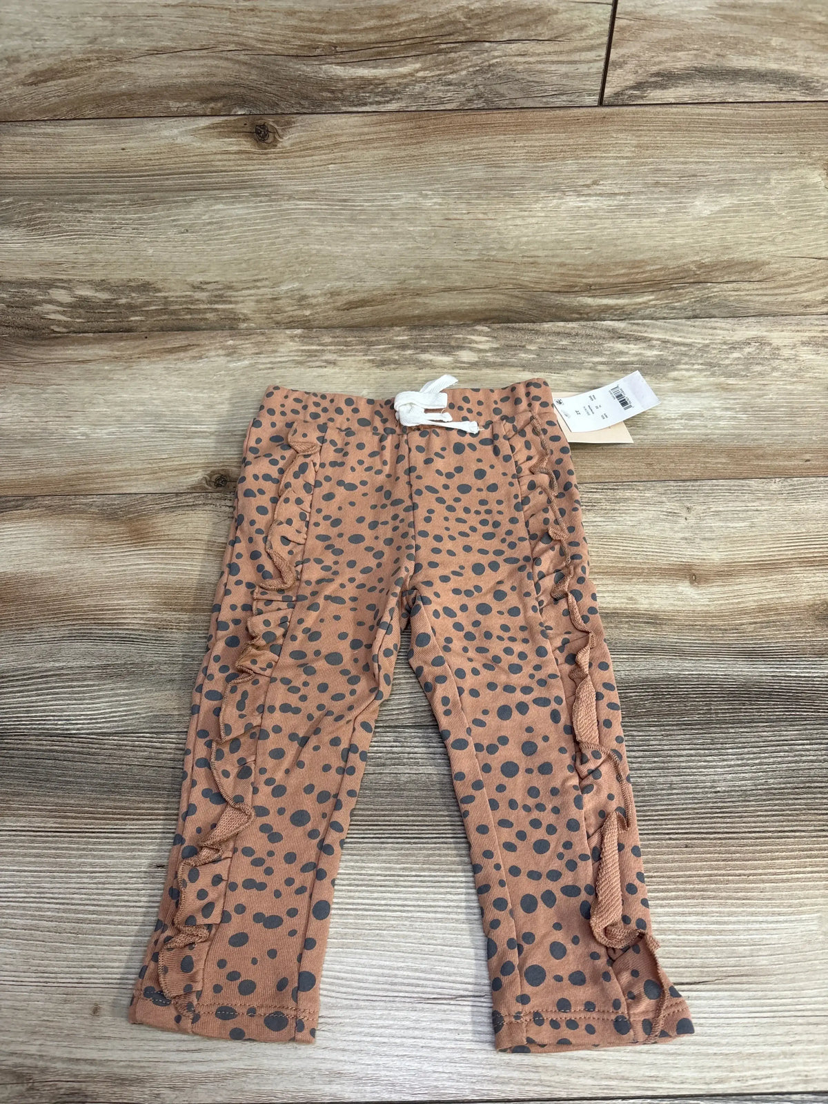 Infant brown polka dot ruffle pants with drawstring, laid flat on wooden background