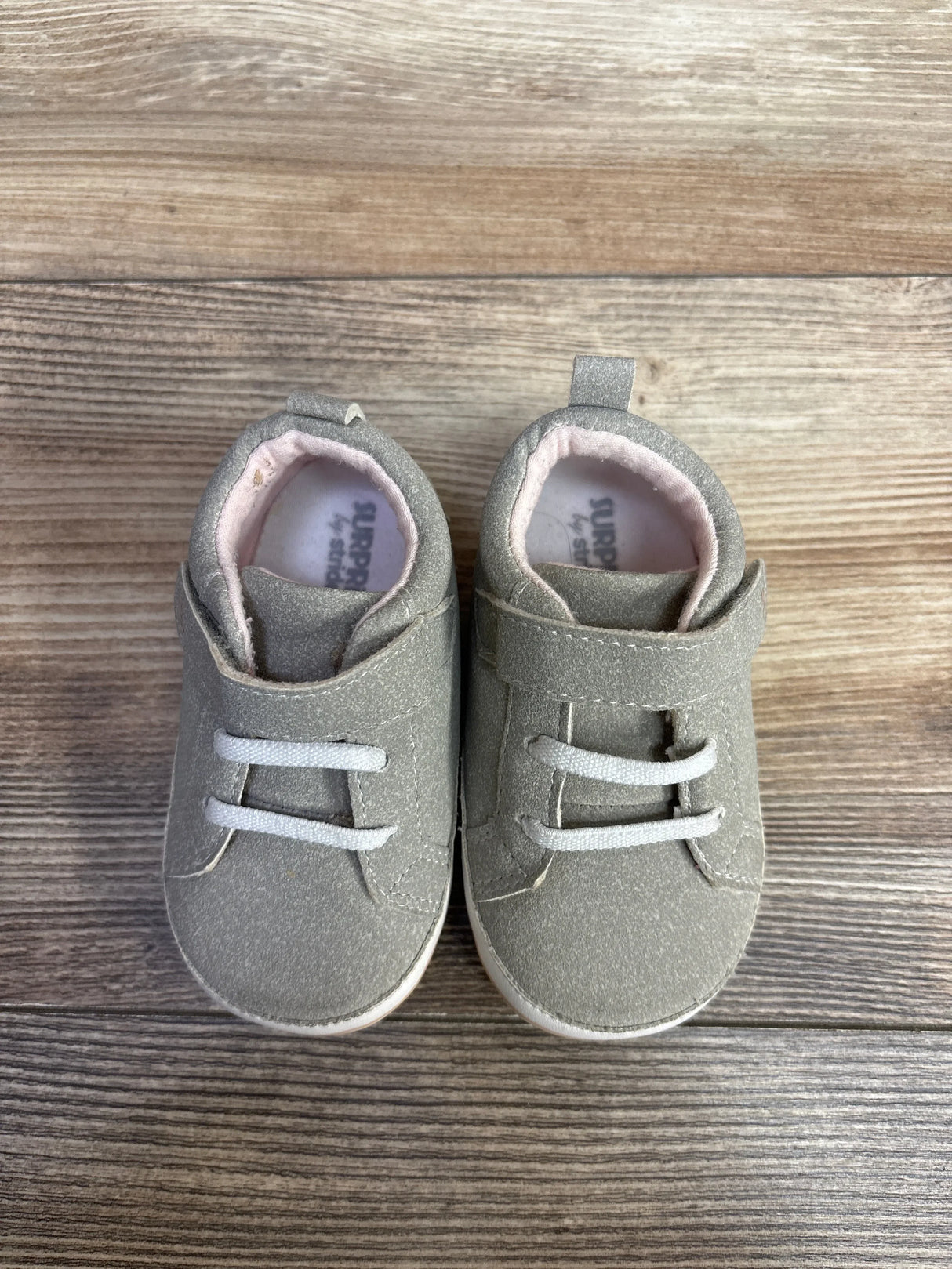 Pair of gray baby shoes with white laces and pink inner lining on wooden floor