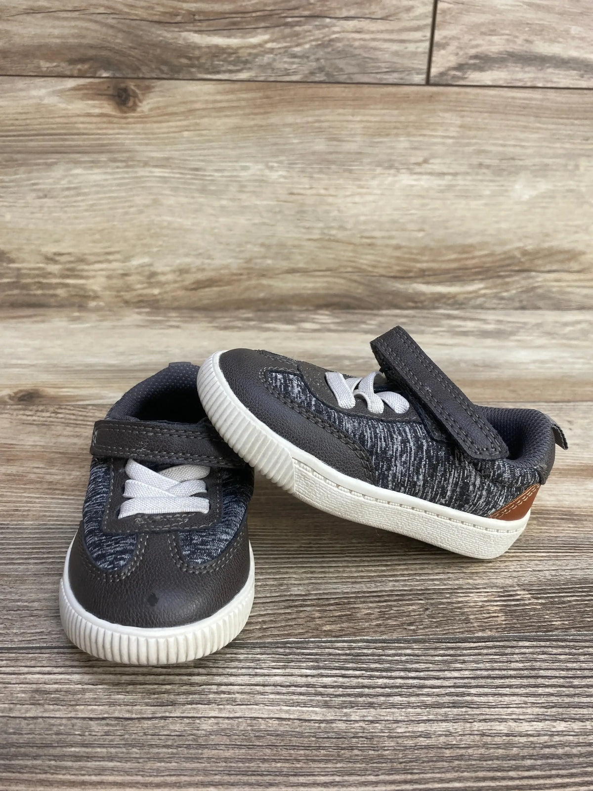 Pair of gray and white toddler sneakers with Velcro straps on wooden floor