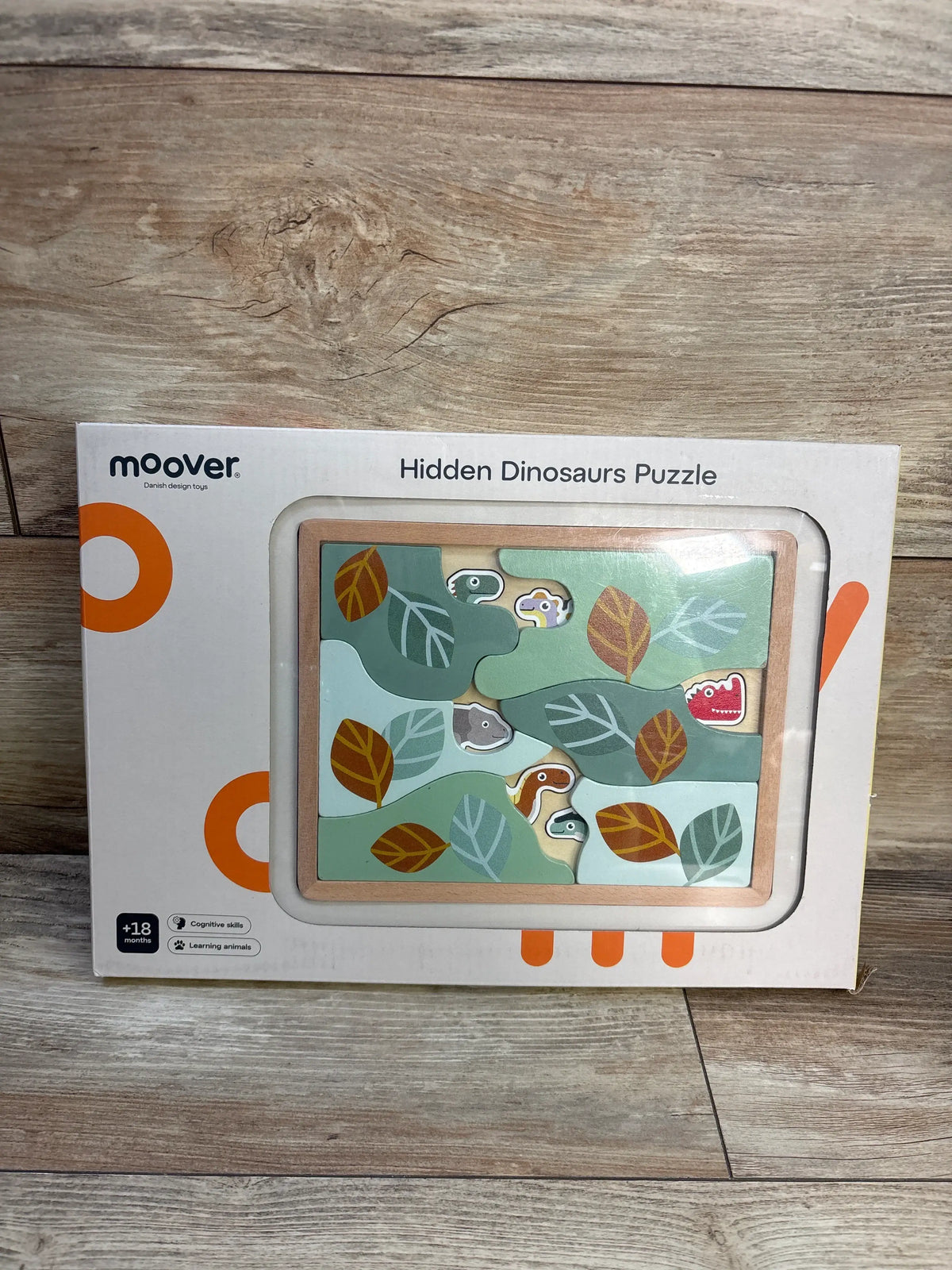 Front view of Moover Hidden Dinosaur Puzzle showcasing layered dinosaur pieces in a box on a wood floor