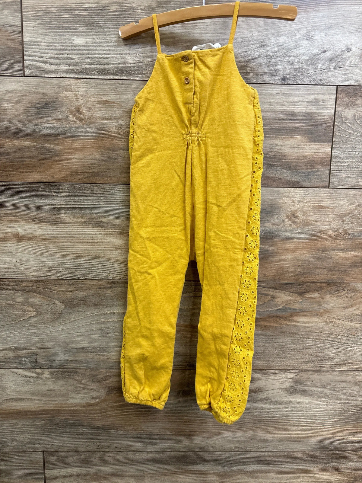 Front view of Zara yellow sleeveless eyelet jumpsuit showcasing button front and eyelet side panels on a wooden hanger
