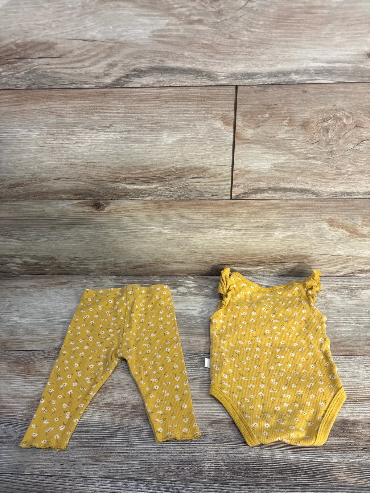 Front view of Kit + Pearl two-piece yellow ribbed bodysuit and pants set showcasing white floral print on a wood floor