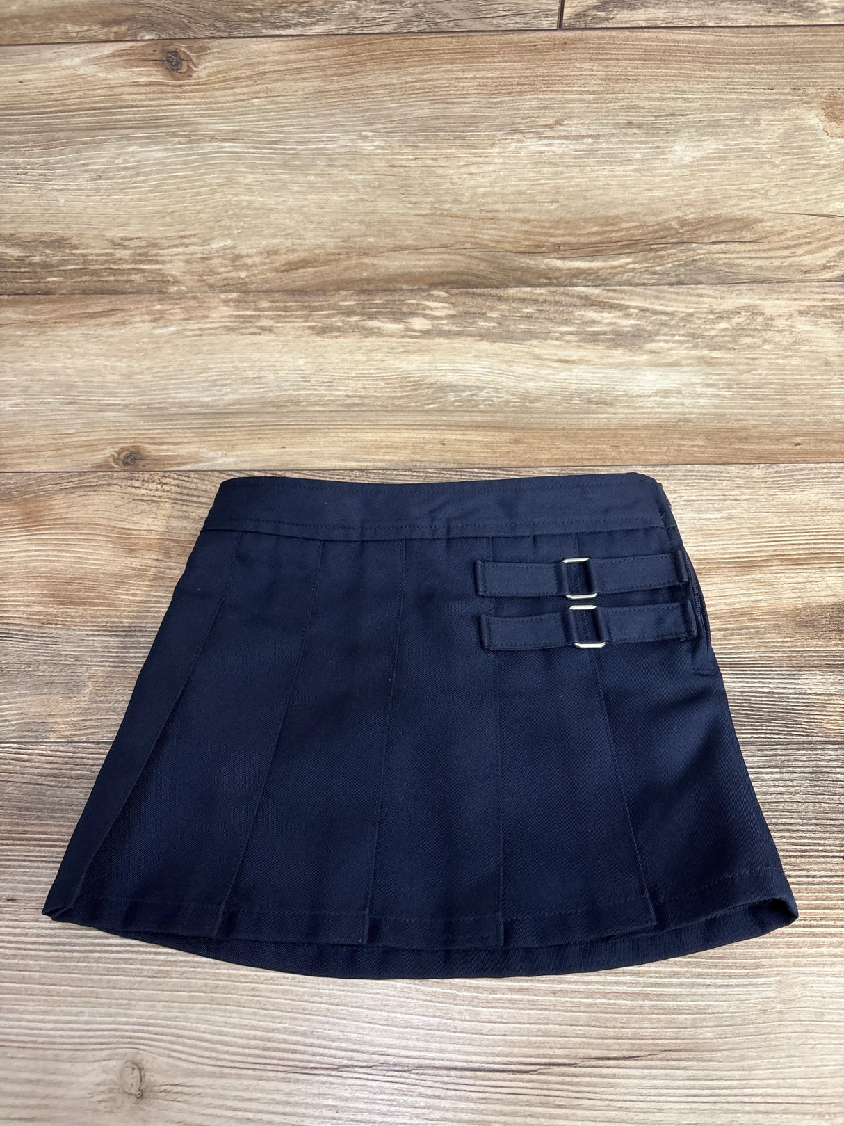 Navy blue pleated toddler skirt with adjustable side buckle straps on wood background