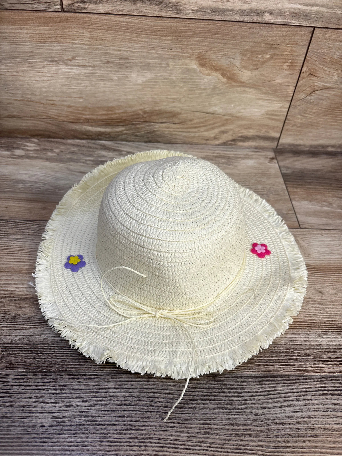 Top view of Juncture floral straw bucket hat showcasing fringed brim, flower accents, and chin tie on a wood surface