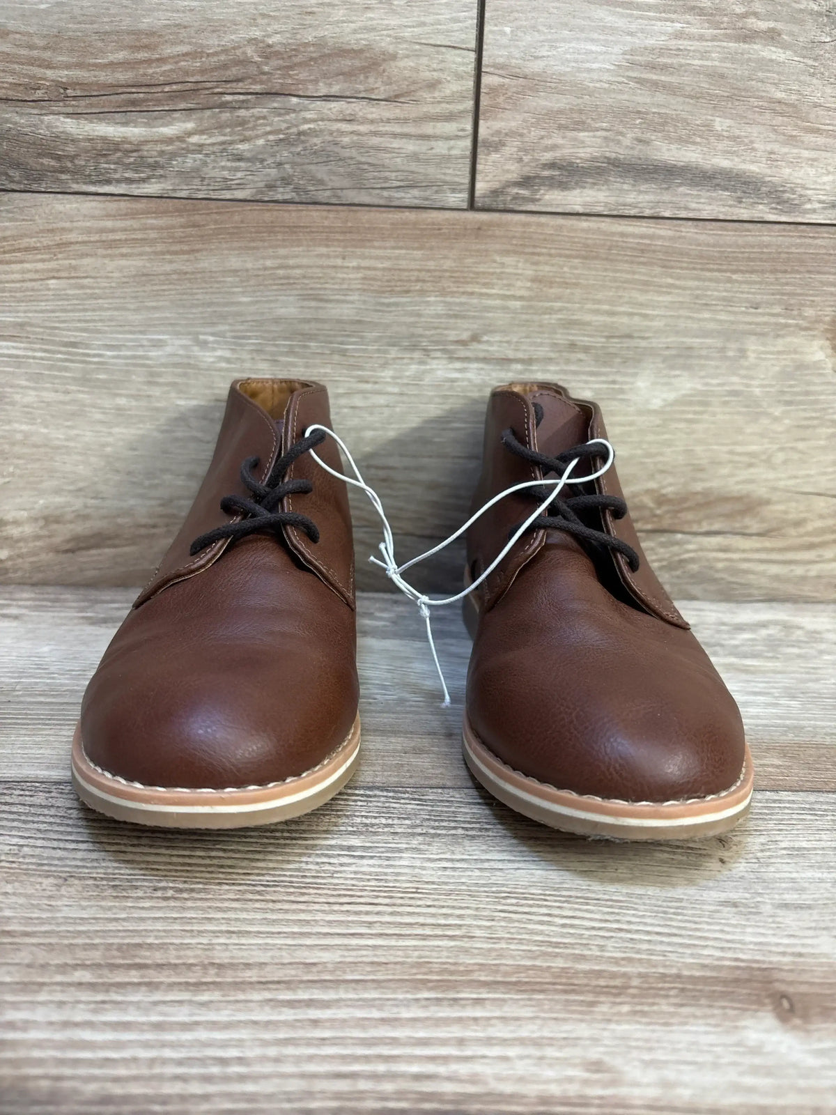 Front view of Cat and Jack Filip toddler brown leather boots showing lace up chukka style and rubber soles on wood floor
