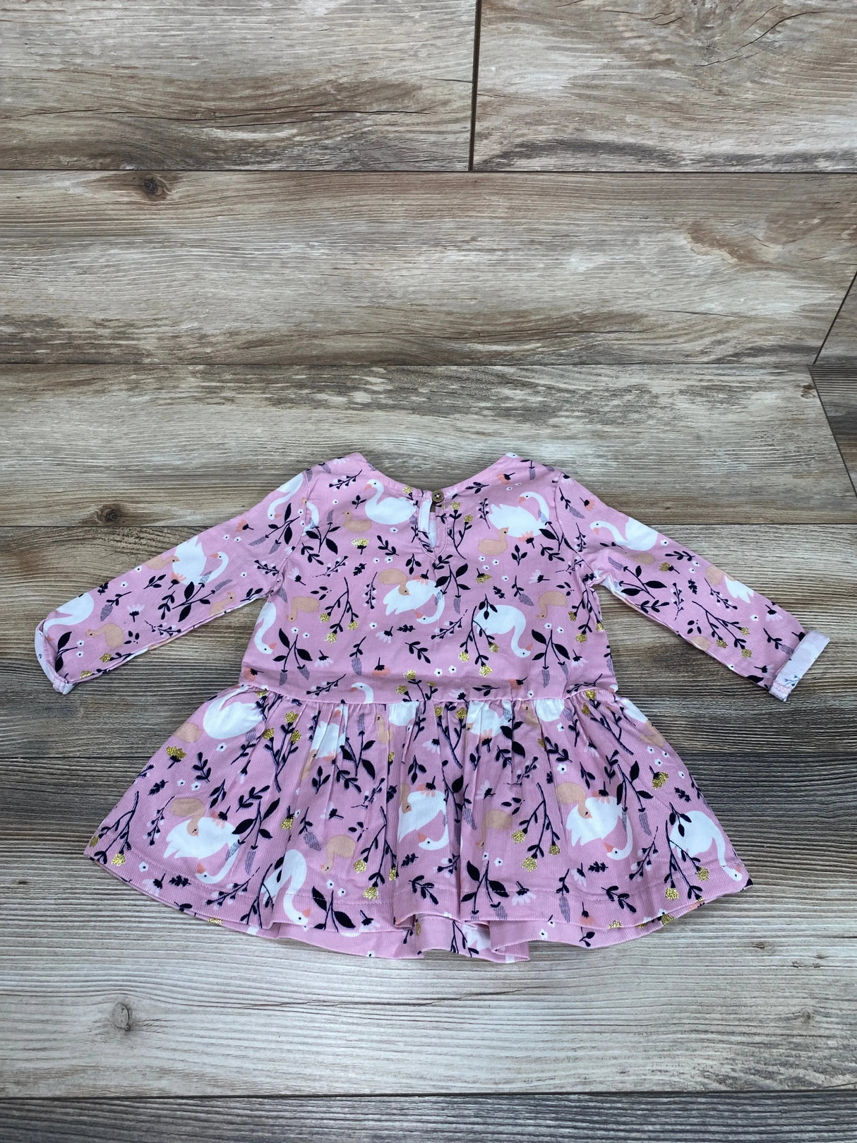 Flat lay of pink Anko baby long-sleeve dress showcasing gathered skirt and white swan and floral print on wood floor background