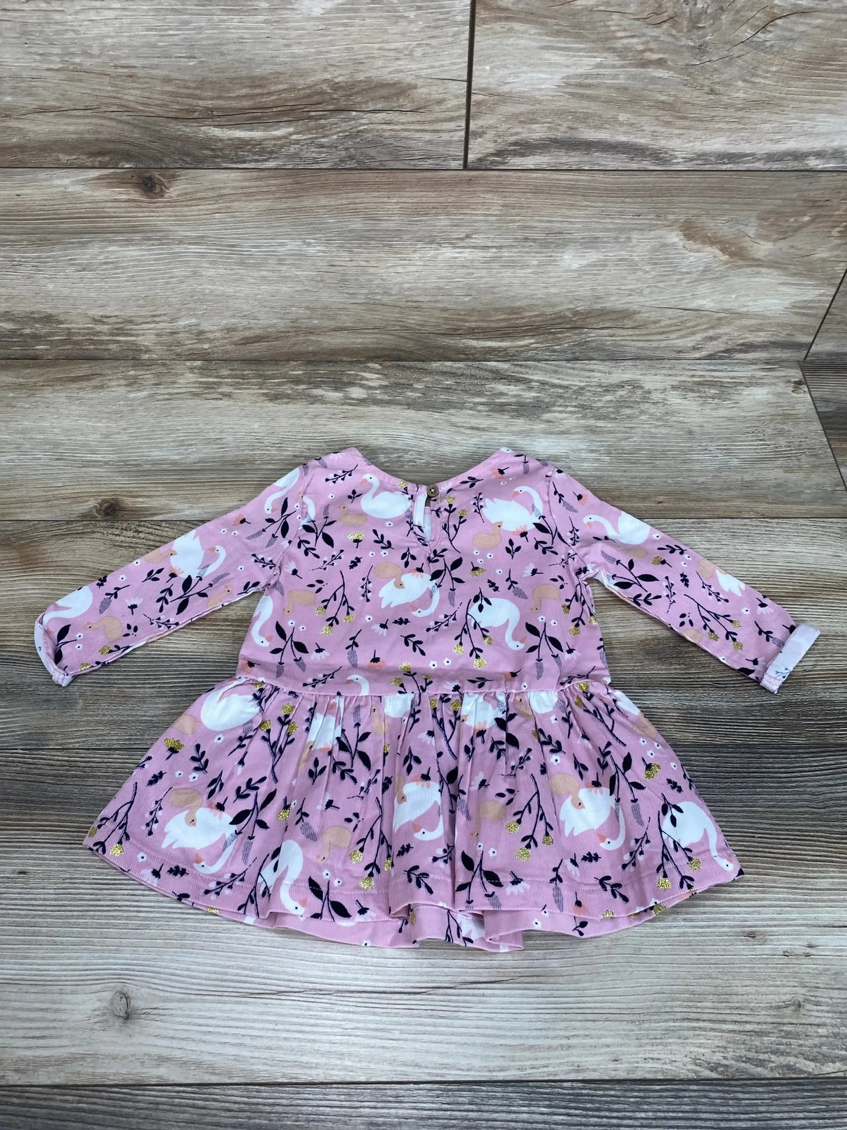 Flat lay of pink Anko baby long-sleeve dress showcasing gathered skirt and white swan and floral print on wood floor background