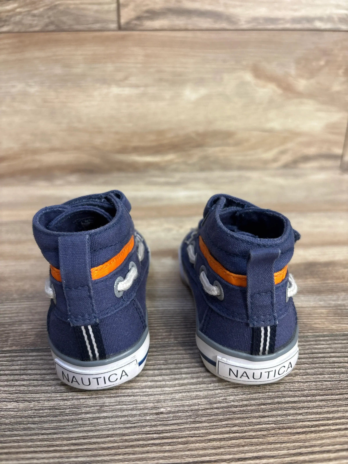 Back view of navy blue Nautica baby shoes with orange stripe on wooden surface