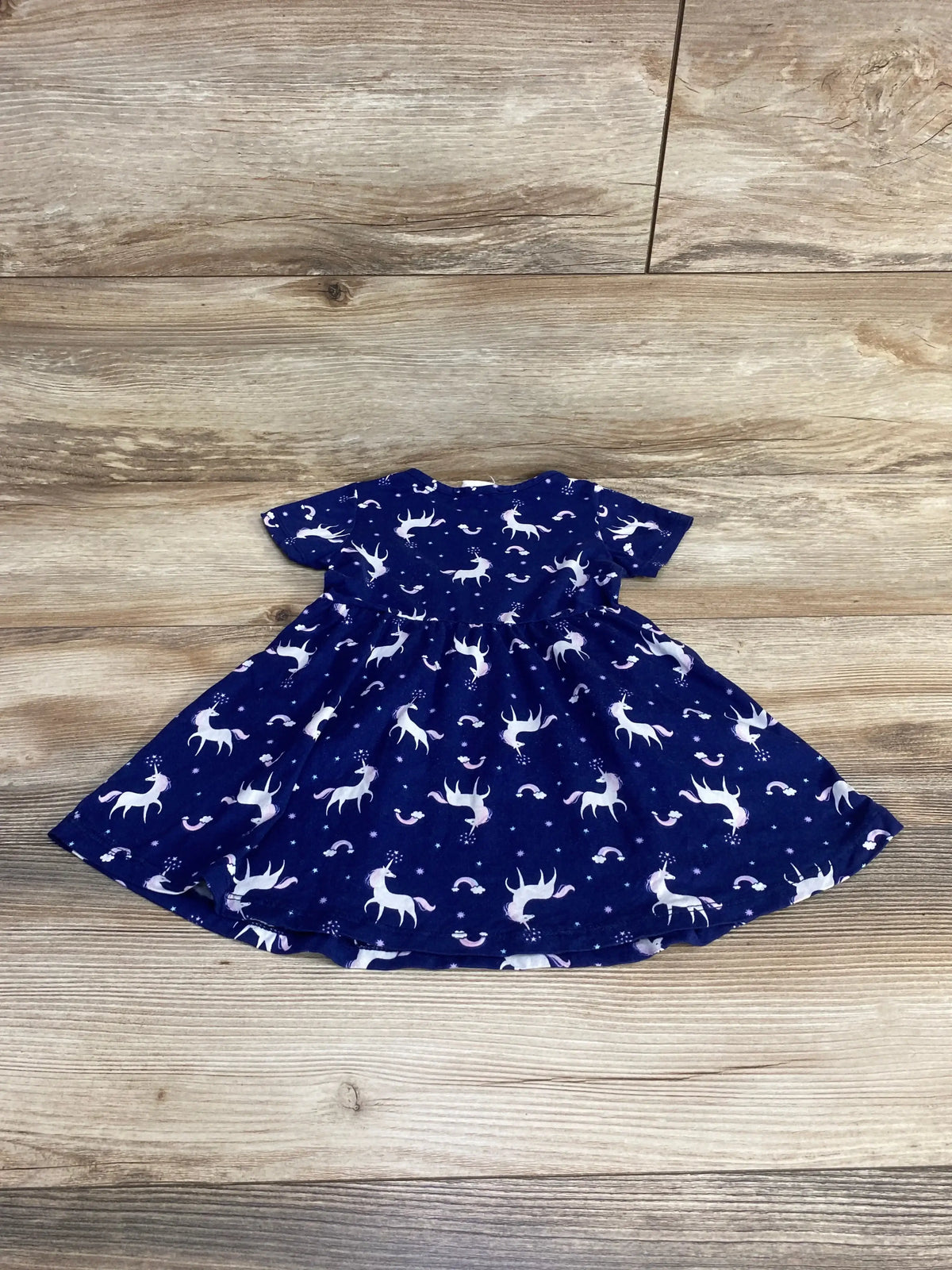 Flat lay of Emma & Elsa blue 2T unicorn dress showing short sleeves and gathered skirt on wood floor background