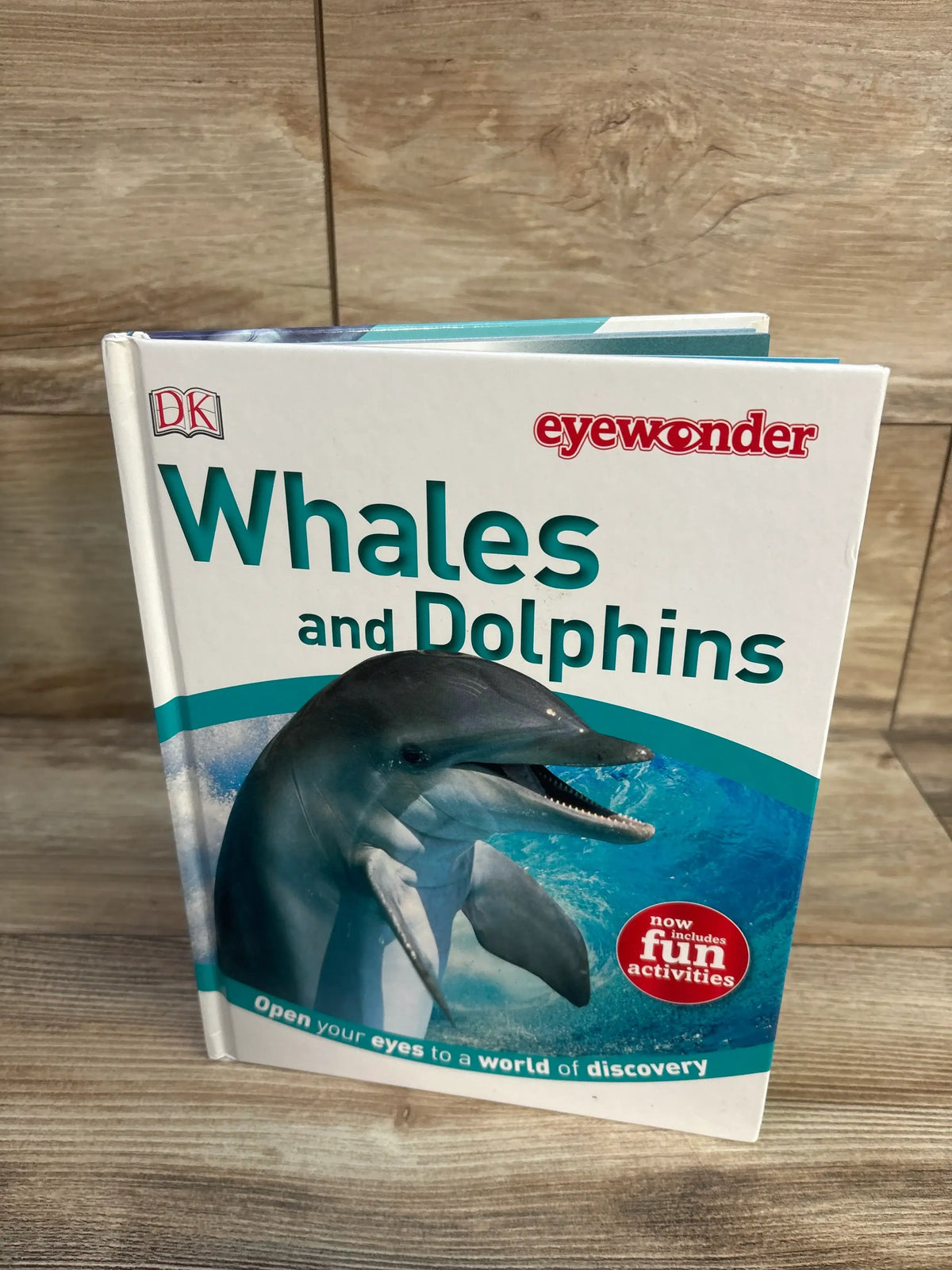 Front view of Eye Wonder: Whales and Dolphins hardcover showcasing a dolphin underwater and a fun activities badge