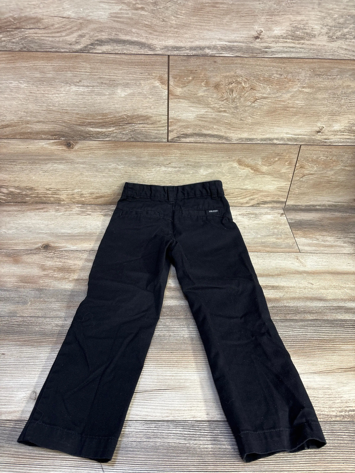 Back view of Volcom VMonty toddler pants in black showcasing straight legs and elastic waistband with wood plank background