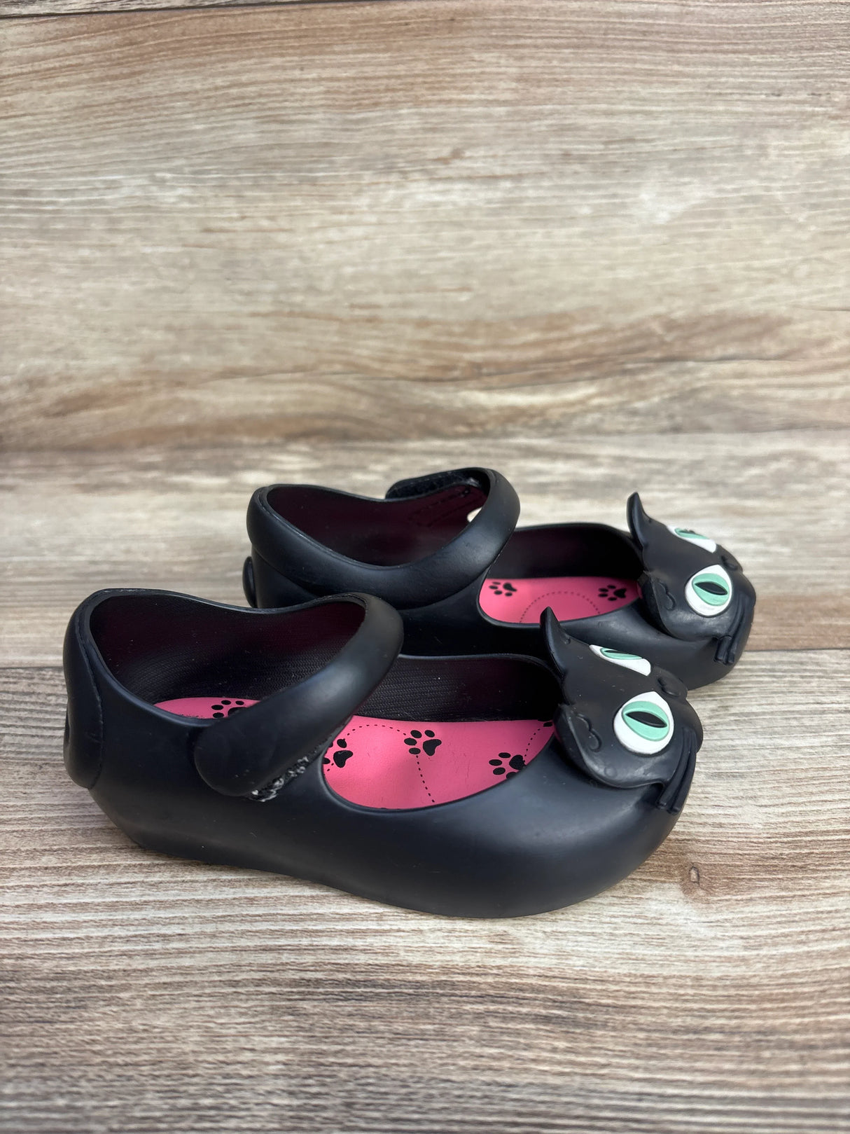 Black children's Mary Jane shoes with cat face design and pink paw print insoles on wooden surface