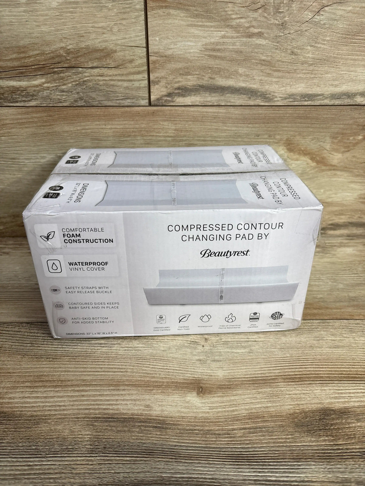 Front view of boxed Beautyrest contoured changing pad showing waterproof vinyl cover and foam core on wood floor