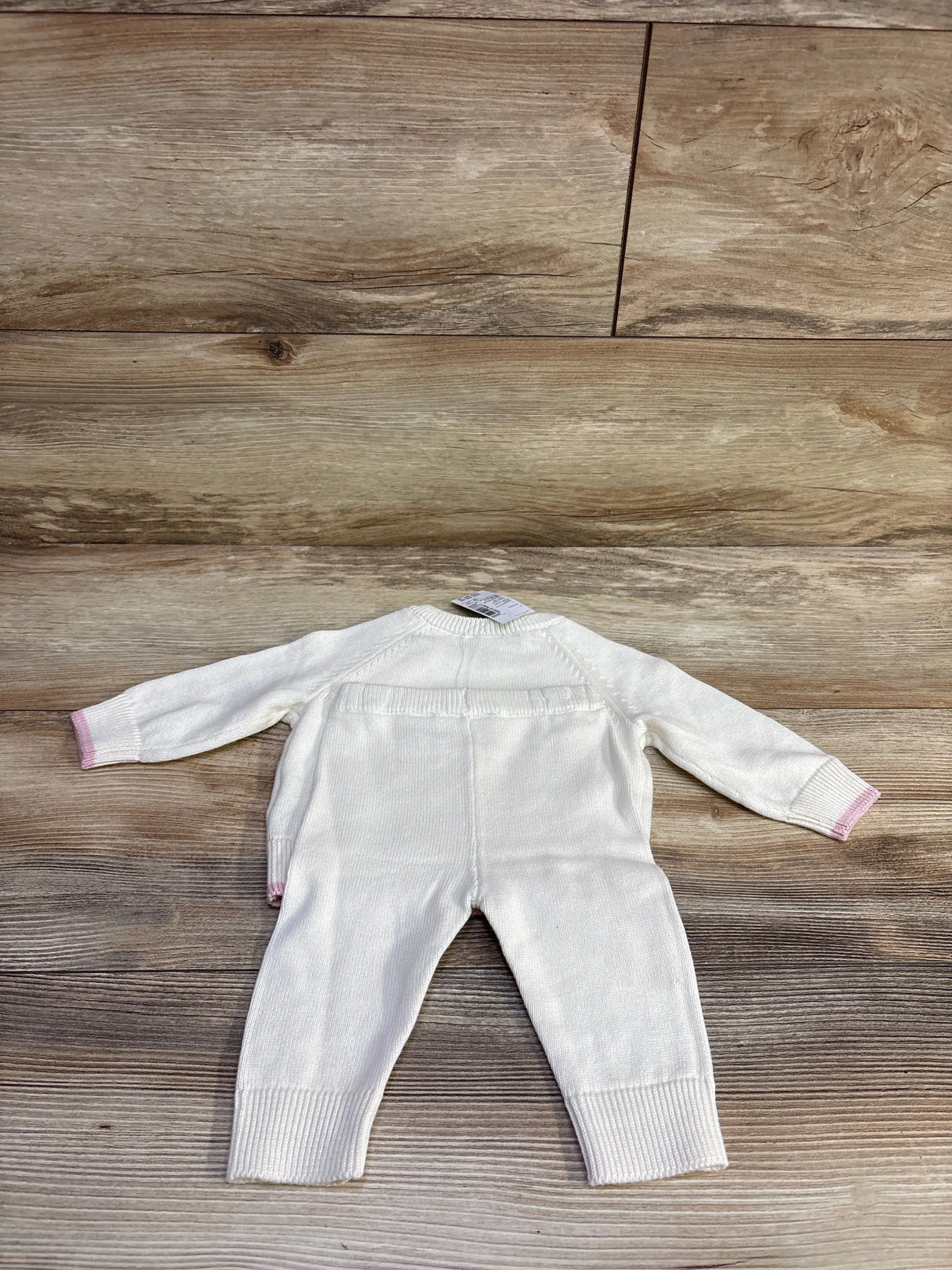 Back view of infant two-piece knit sweater and pants set in ivory with pink-trim cuffs laid flat on wood surface