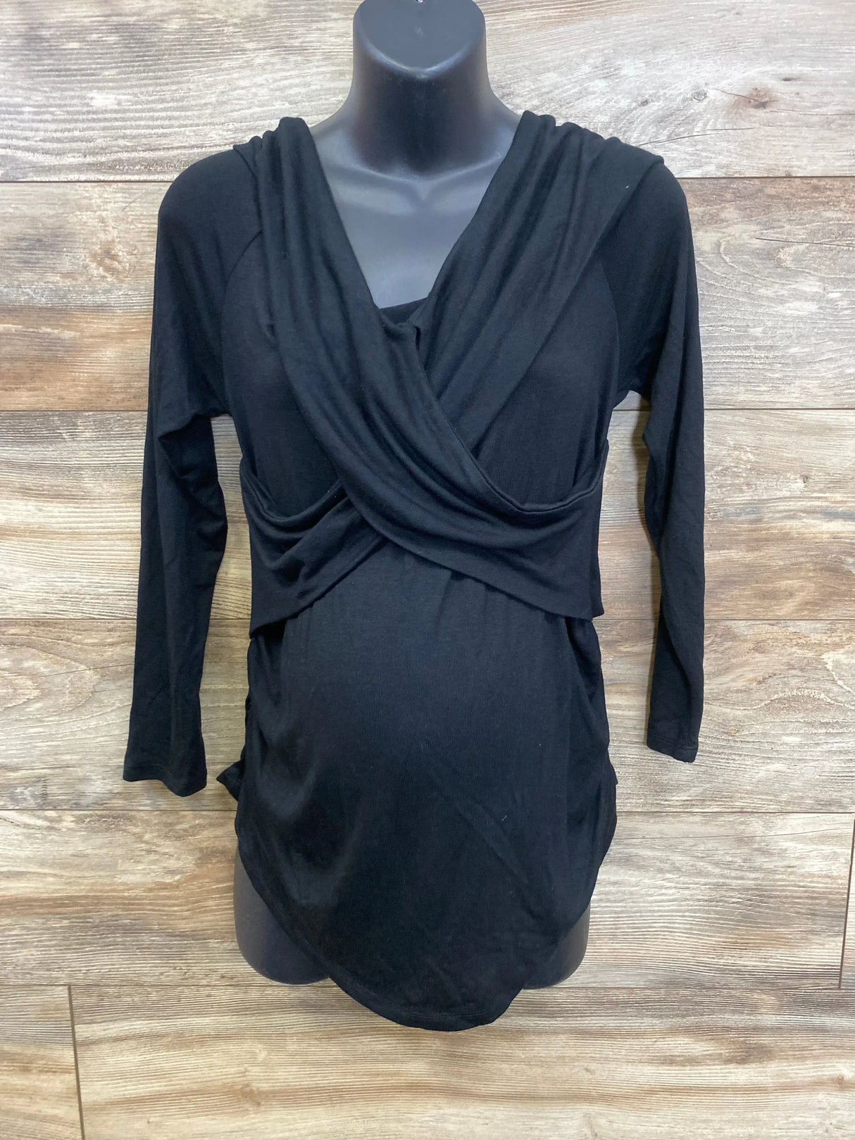 Black long sleeve maternity top with draped front on mannequin, wood background