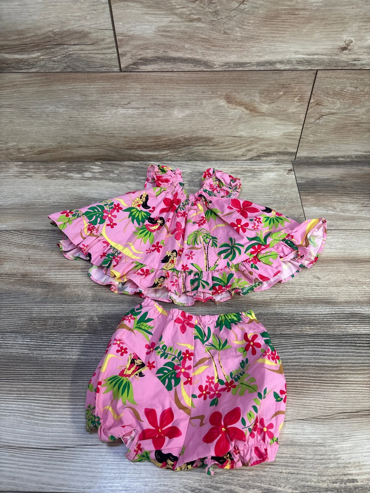 Flat lay of RJC Hula Girl 2-piece cabana set showcasing ruffled off-shoulder top and elastic-waist bloomers on light wood background, size 6M
