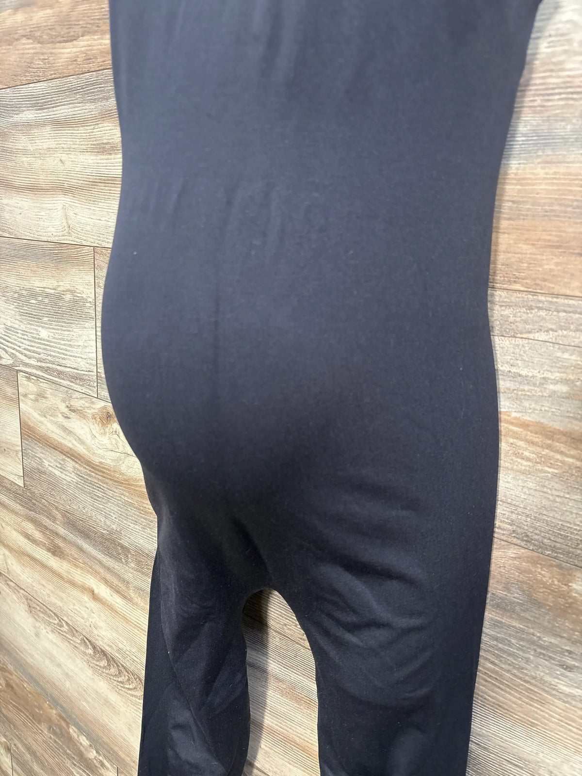 Close-up view of black maternity nursing tank jumpsuit laid flat on a wood-look floor