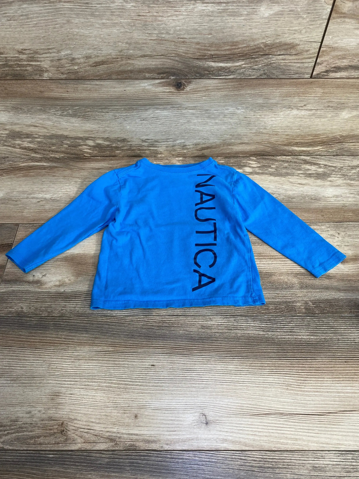 Flat lay of Nautica toddler long-sleeve blue shirt size 2T showcasing vertical NAUTICA logo with light wood background