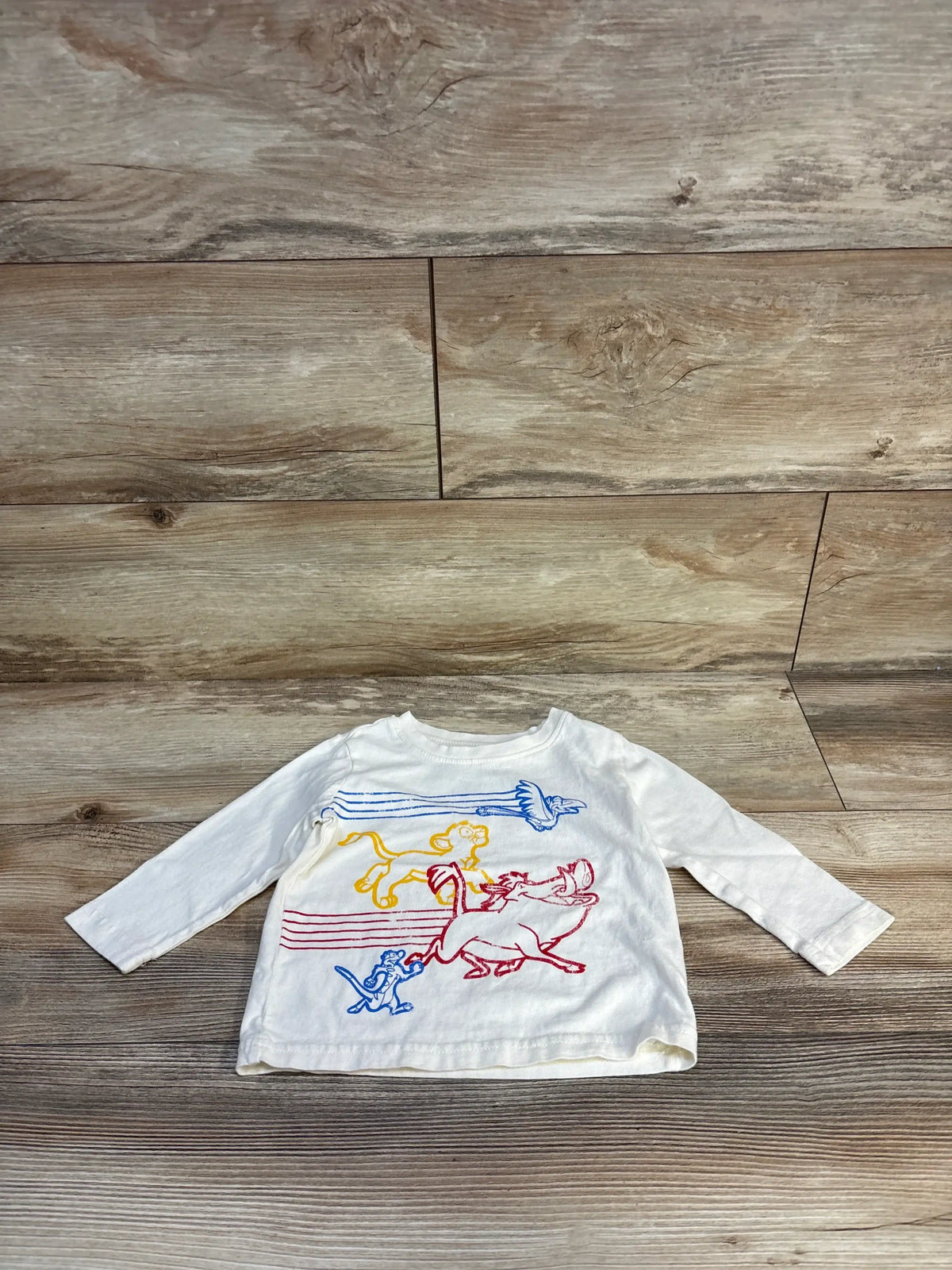 White long sleeve toddler shirt with colorful Lion King characters graphic, laid on wood floor