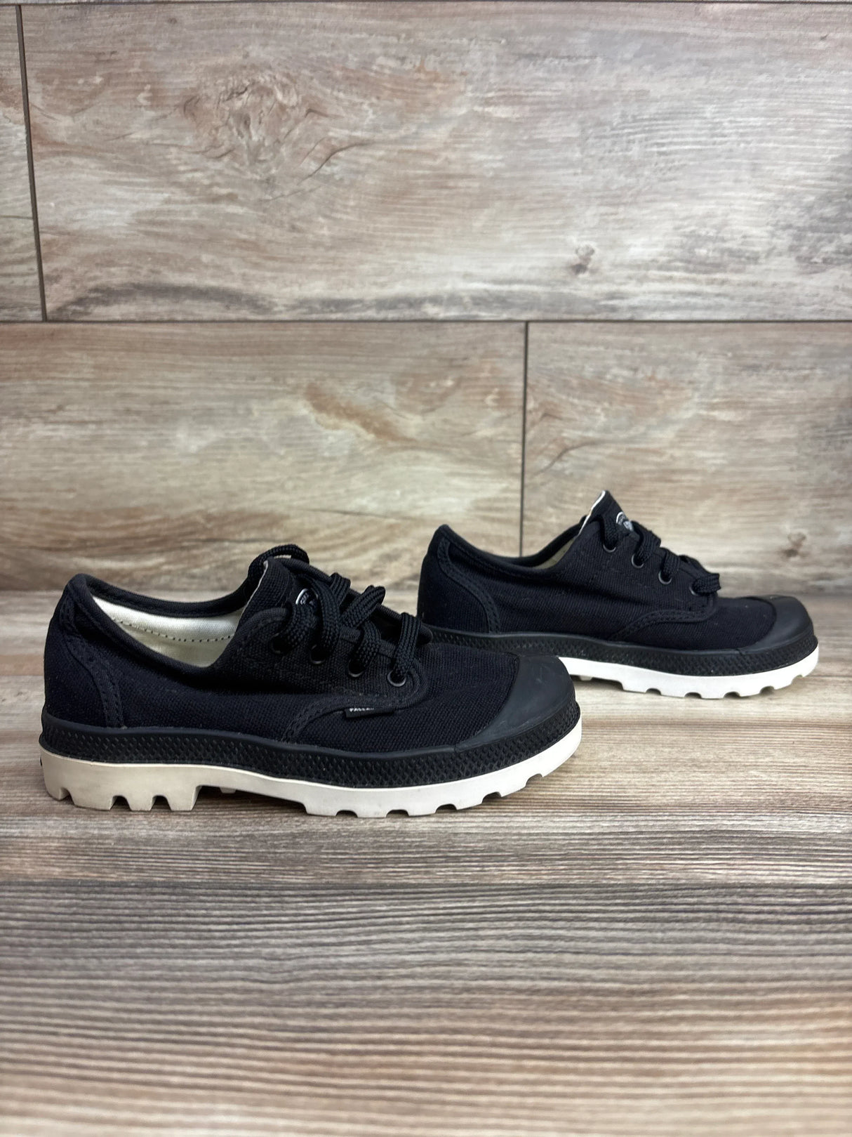 Pair of black canvas kids shoes with white rubber soles on wooden surface