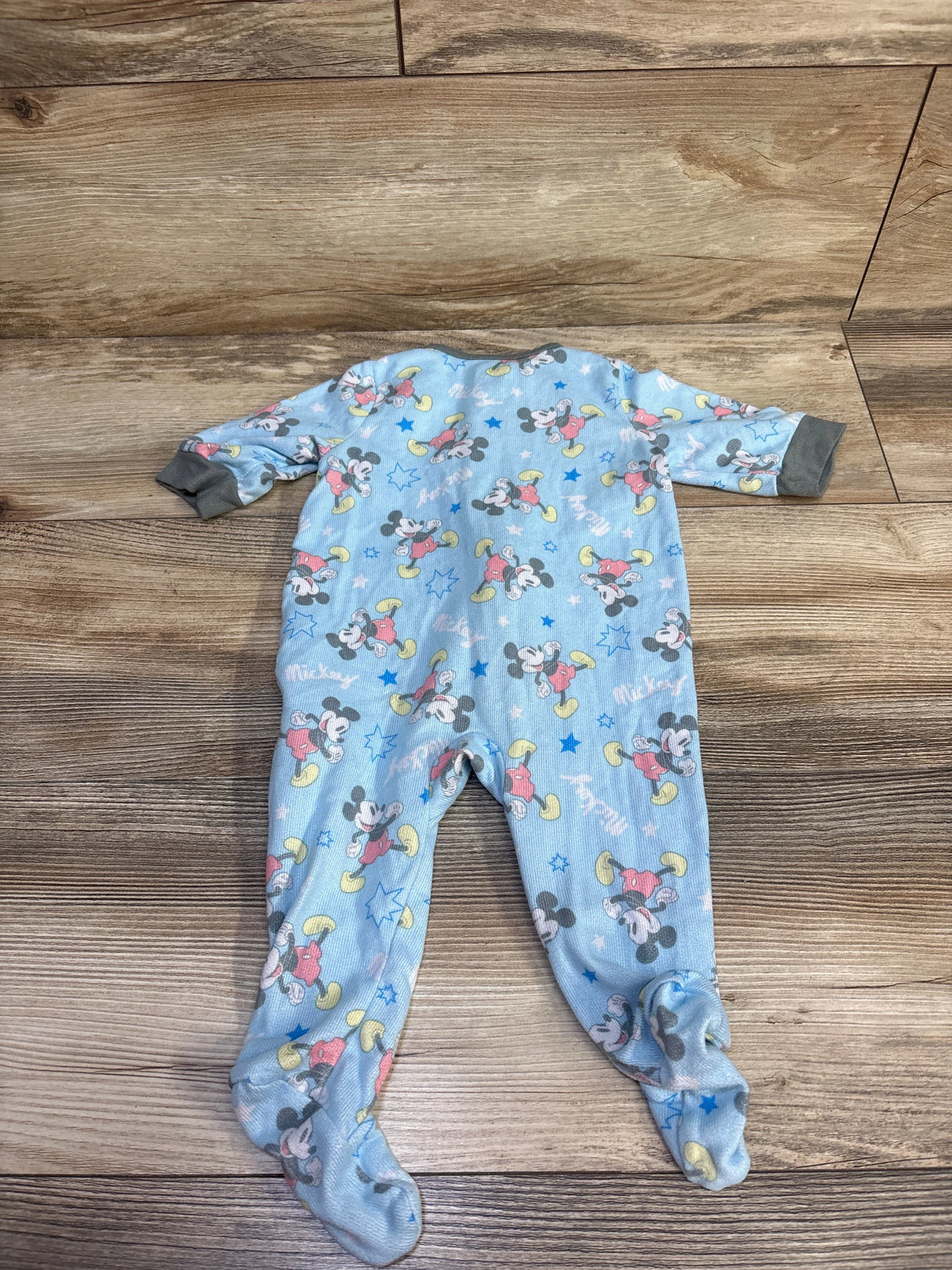 Flat-lay of blue Mickey Mouse footed sleeper showing all-over Mickey print and gray cuffs on wood background