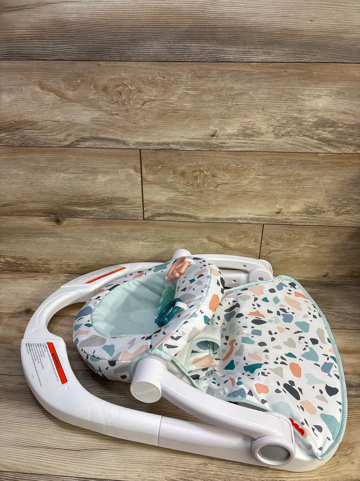 Angled view of Fisher Price Sit-Me-Up Floor Seat in Pacific Pebble showcasing its patterned seat and folded frame on a wood floor
