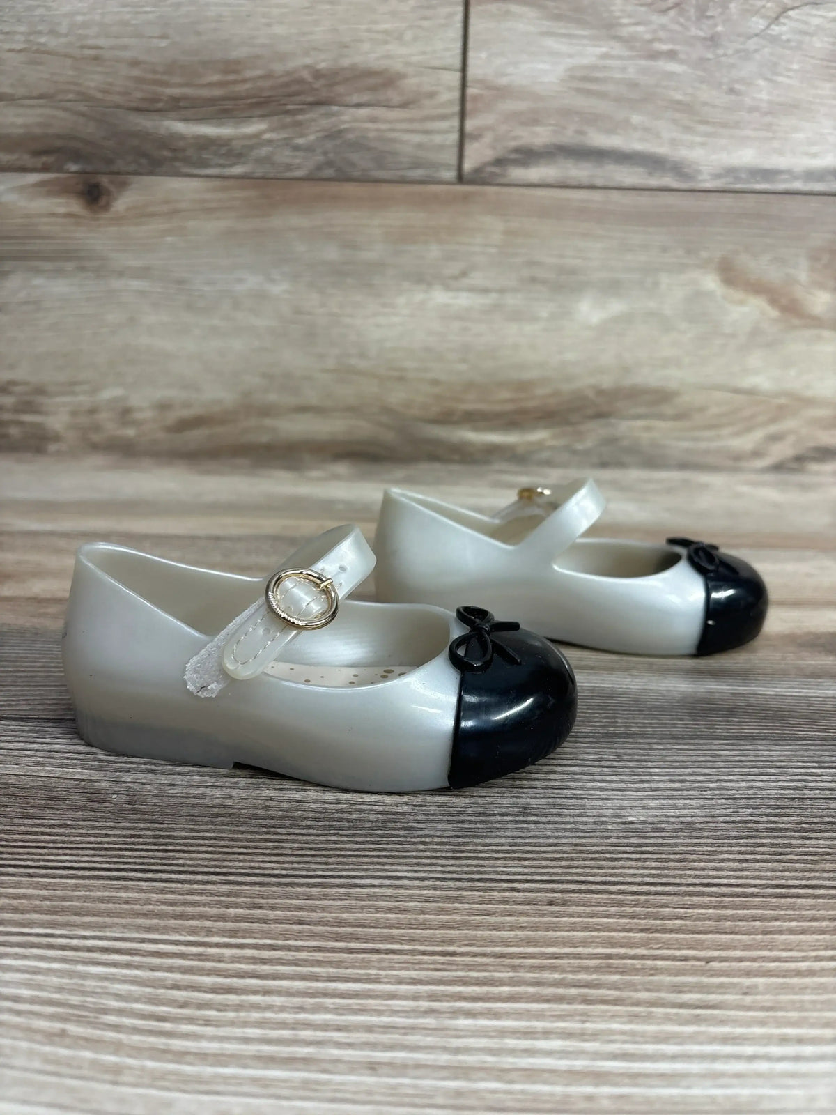 Pair of white and black toddler Mary Jane shoes with gold buckles on wooden floor