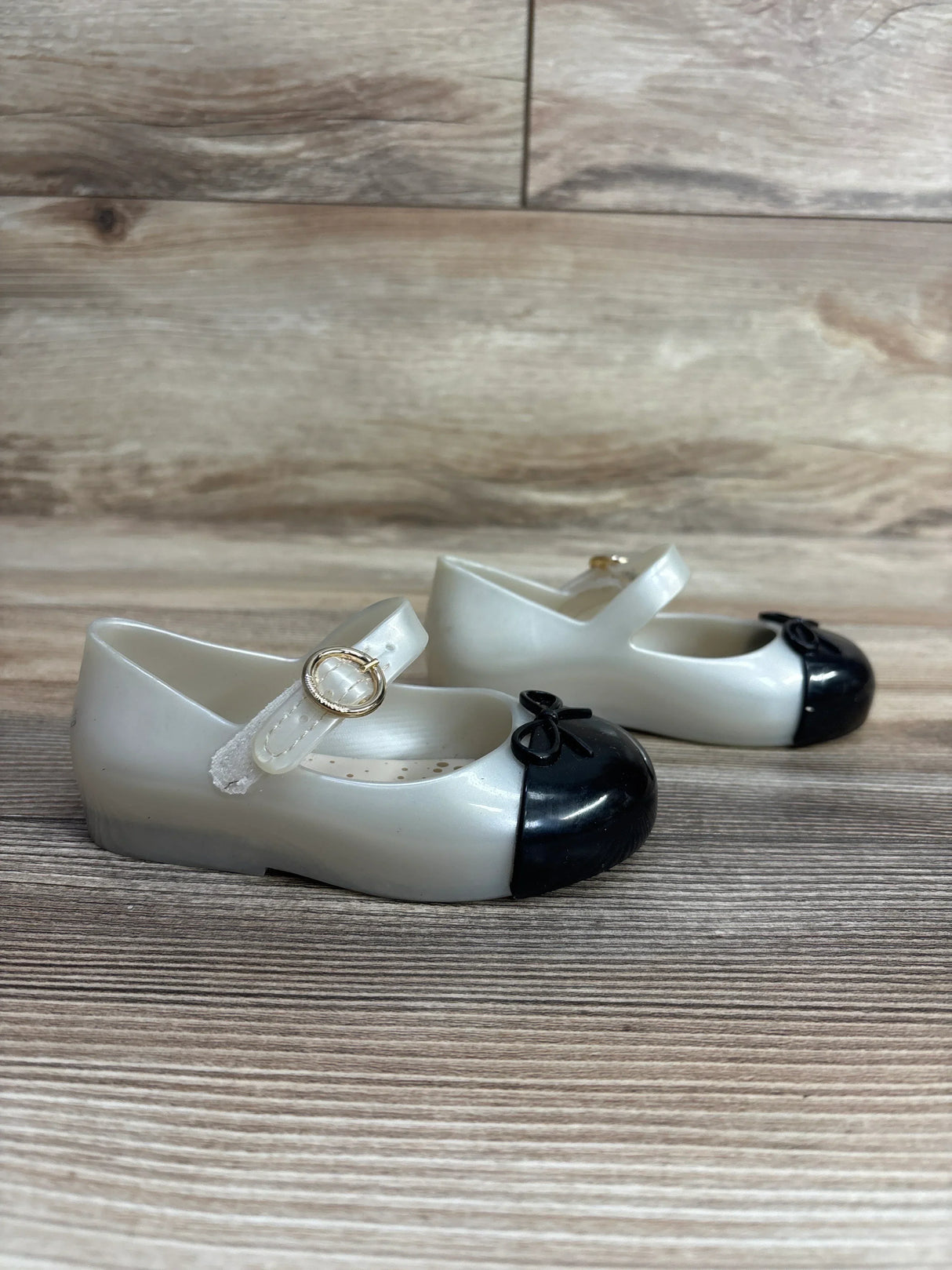 Pair of white and black toddler Mary Jane shoes with gold buckles on wooden floor