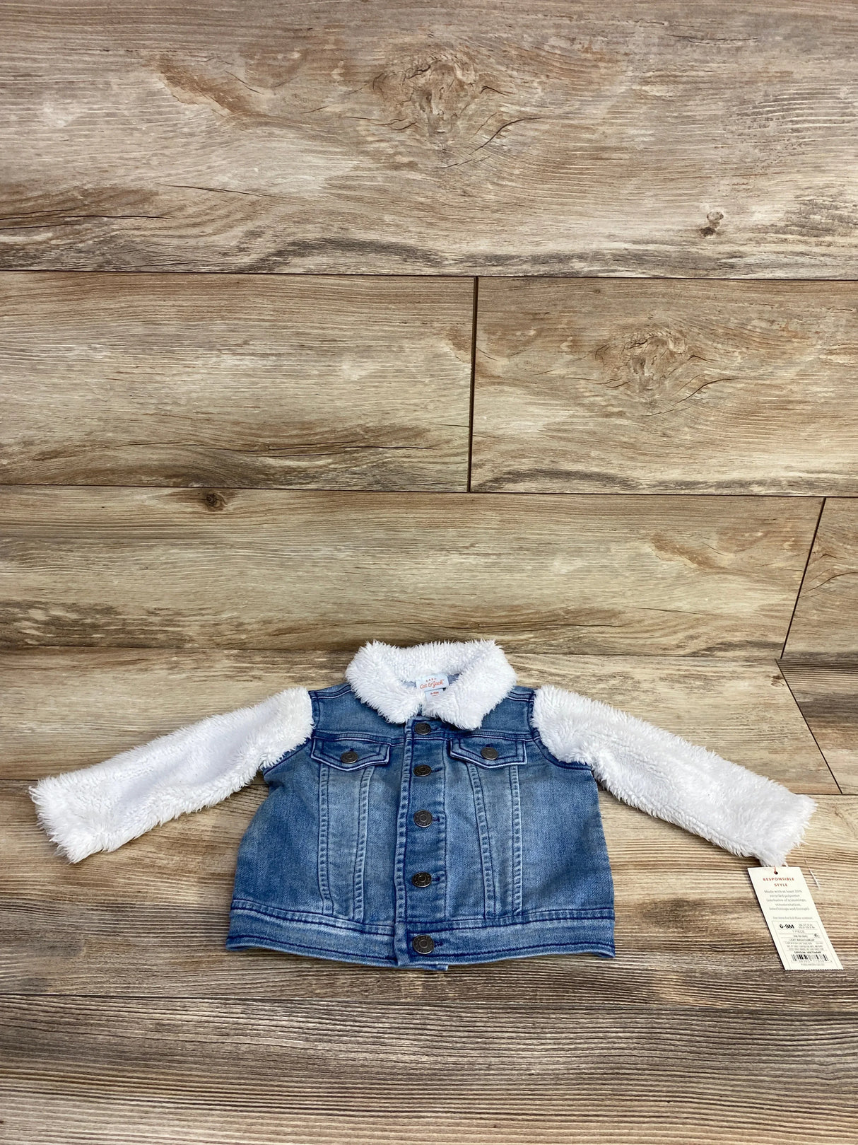 Baby denim jacket with white fuzzy sleeves and collar laid flat on wooden surface