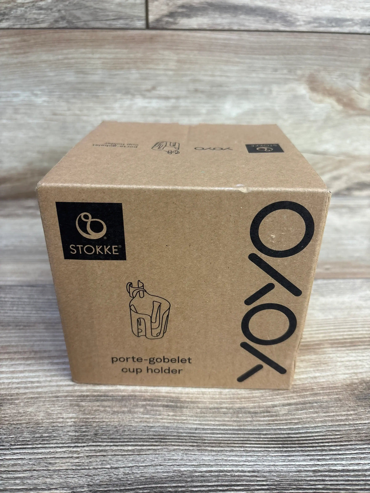 Front view of Stokke Yoyo cup holder box showing printed Yoyo logo and product sketch on wooden tabletop background