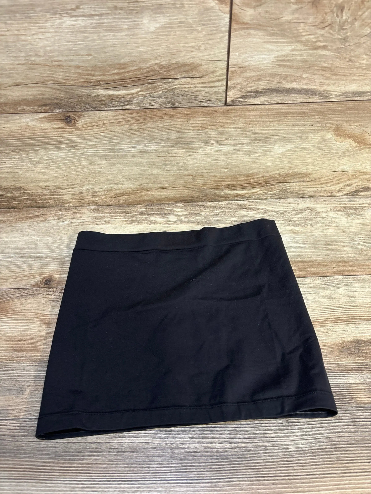 Top-down view of black Ingrid & Isabel maternity belly band showcasing stretch fabric and elastic waistband on wooden floor